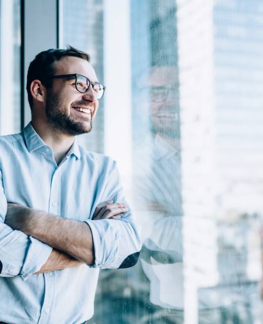 Cheerful male entrepreneur with crossed hands standing near office window view and smiling during work day in company, Caucasian successful corporate boss feeling good from wealthy lifestyle Cheerful male entrepreneur with crossed hands standing near office window view and smiling during work day in company, Caucasian successful corporate boss feeling good from wealthy lifestyle